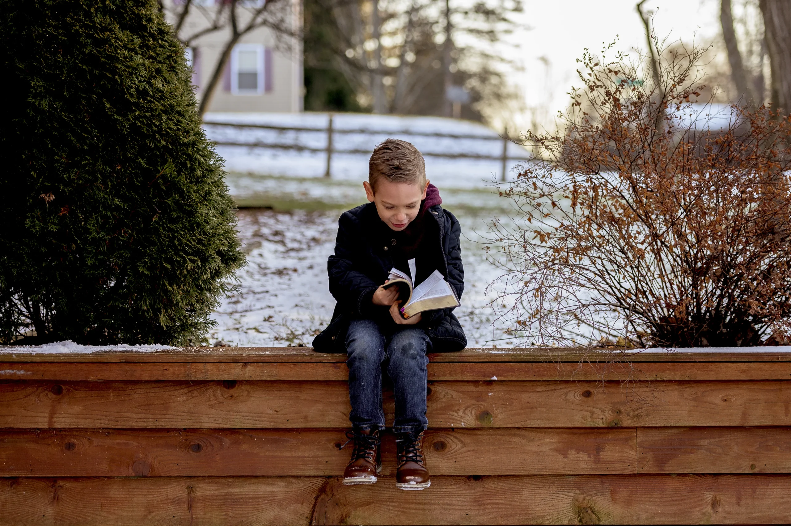 little-boy-sitting-wooden-planks-reading-bible-garden-covered-snow